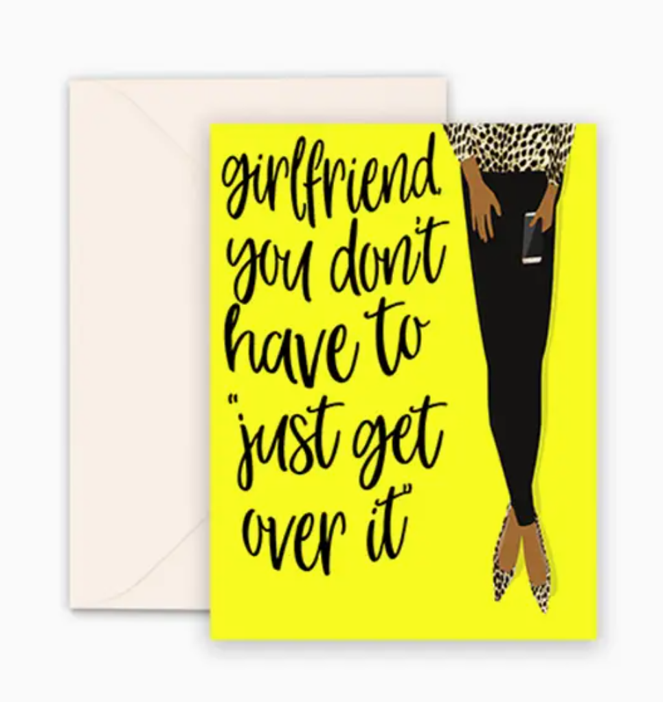 A vibrant yellow greeting card with black text that reads, girlfriend, you don't have to just get over it. and an illustration of a woman's legs wearing an animal-print top, black pants, and high heels. A Kraft brown envelope is included.
