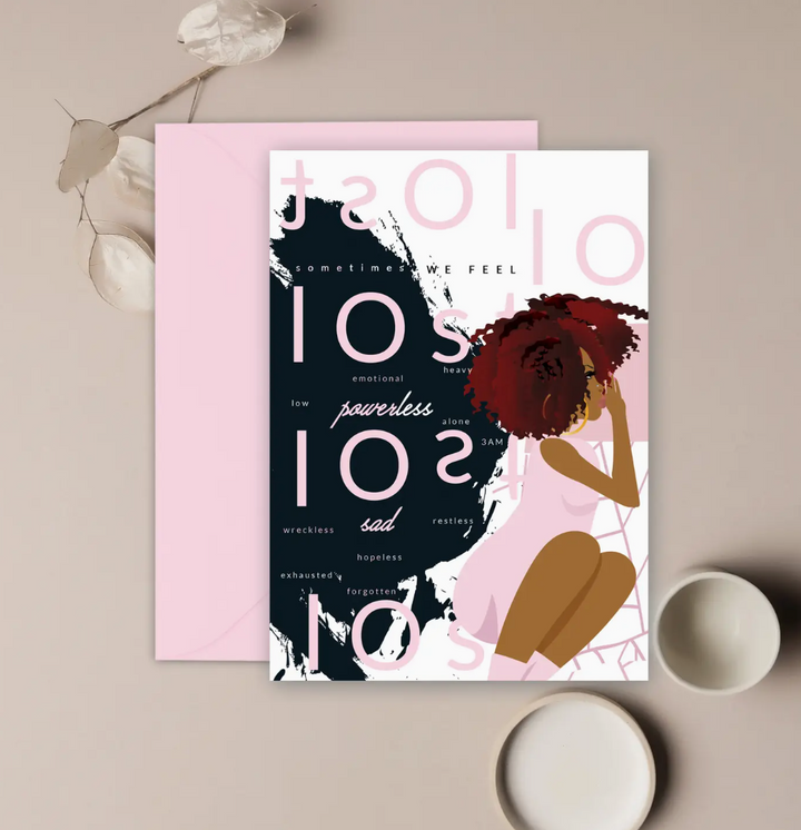 A white greeting card with the illustration of a black woman sitting down and the word "lost" in pink repeated in different directions, as well as words describing different feelings and emotions of uncertainty, placed on a neutral background with a pink envelope and decorative elements.
