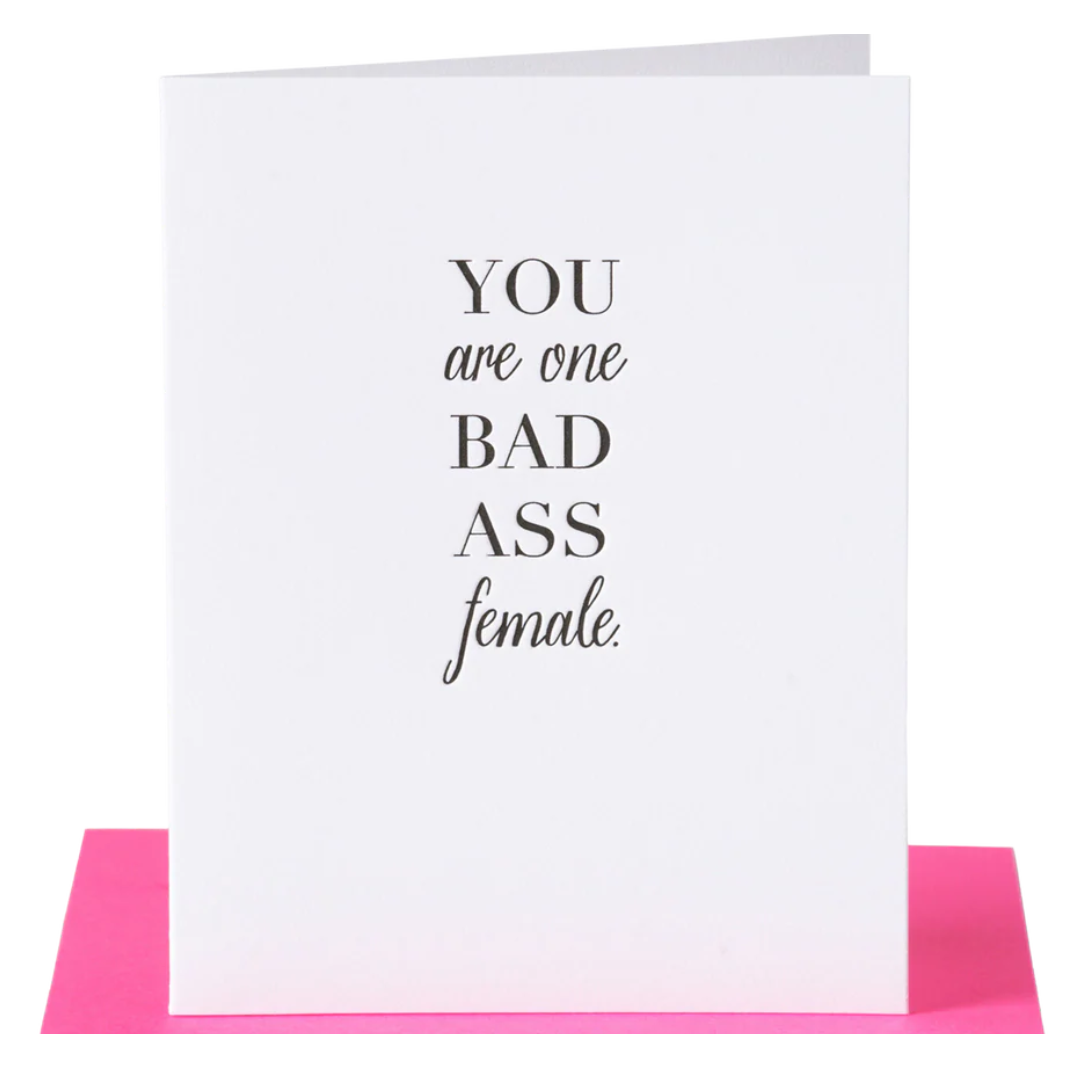White greeting card with black text that reads you are one bad ass female, paired with a hot pink envelope