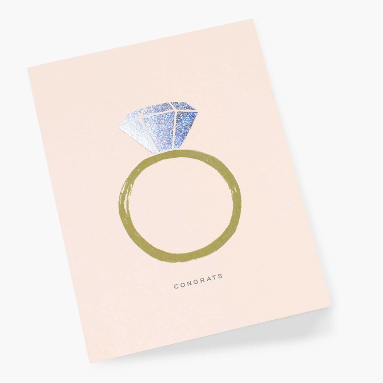 Blush pink greeting card with a gold band diamond ring illustration with iridescent diamond, and the word "Congrats" in grey print below it