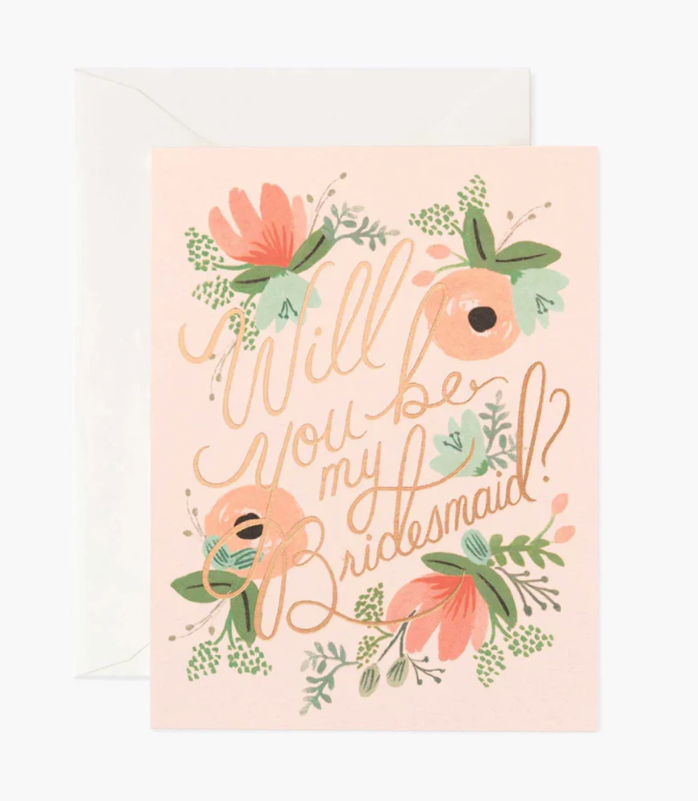Coral-colored greeting card with multi-color floral design and text 'Will you be my maid of honor?' in rose gold foil print with a cream envelope 