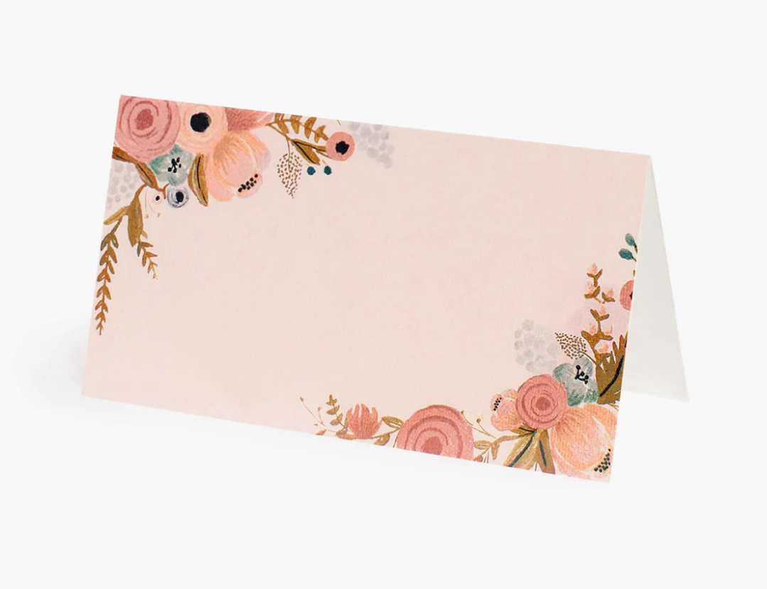 Floral print design in the upper left corner and the lower right corner on a beige-peach colored tent fold-style place card with a white background