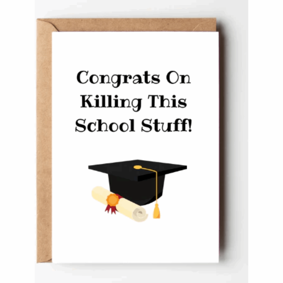 White greeting card with the words congrats on killing this school stuff and the illustration of a black graduate cap, gold tassel, and a rolled diploma and a kraft brown envelope