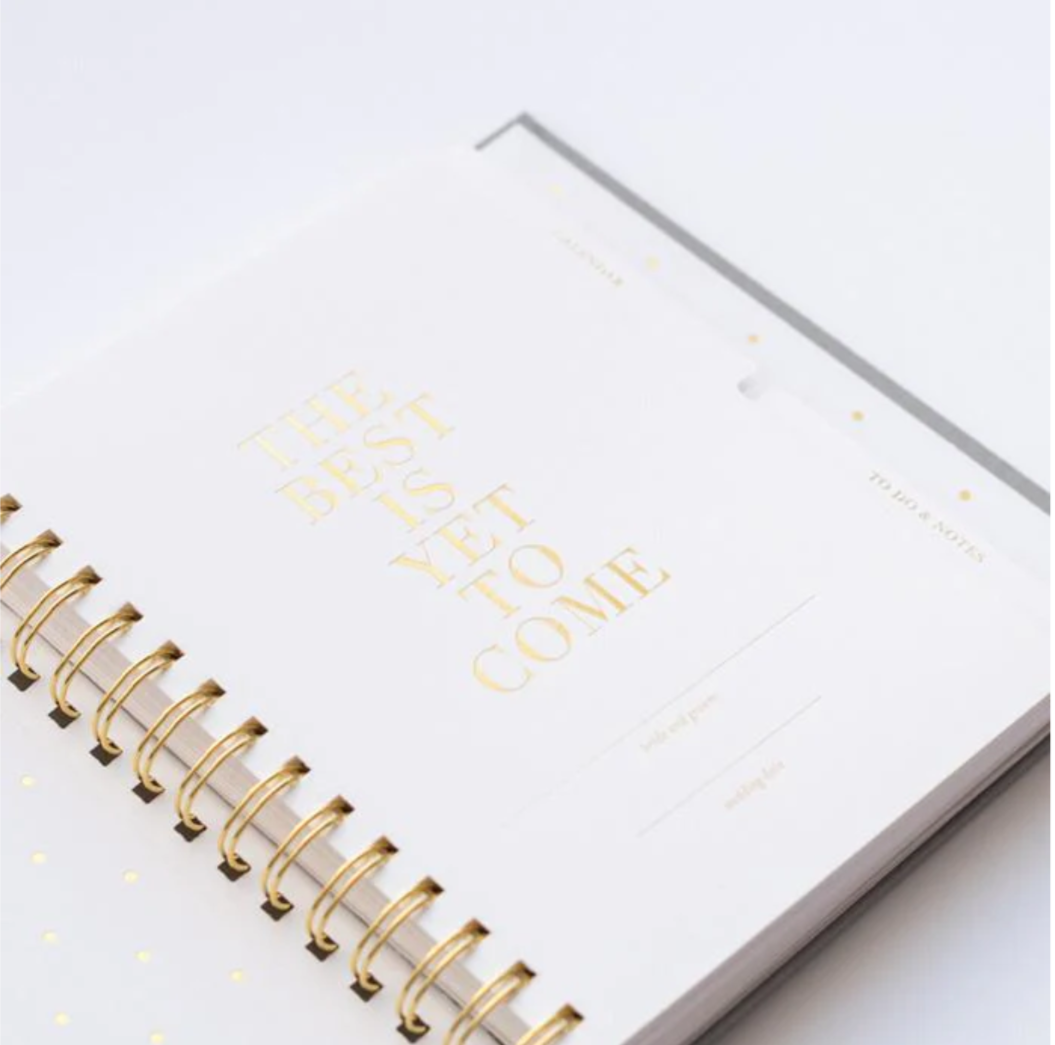 White planner with gold spiral binding and 'The Best Yet to Come' text on a white background
