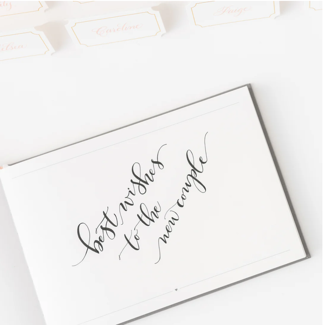 white page in a book with 'Best wishes to the new couple' text with gold trimed white place cards in the background