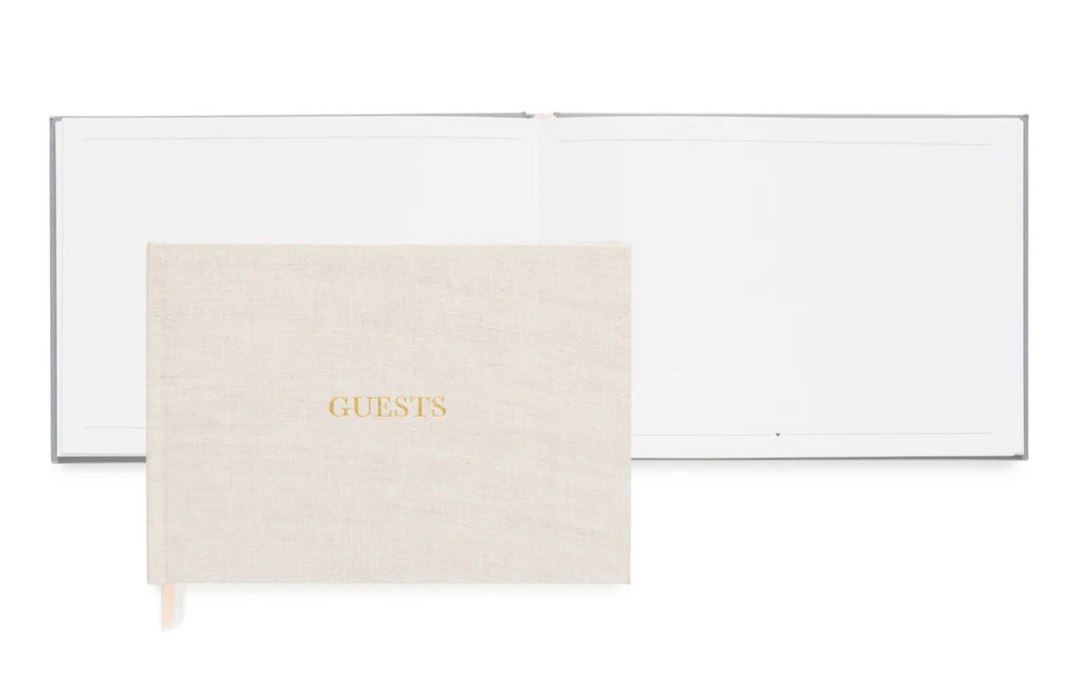 Natural color fabric bookcloth covered guest book with the word guest in gold foil print in front of an open guest book with blank pages