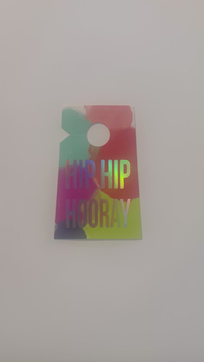 Video of a neon red, aqua, pink, fuchsia, and green splash print gift tag highlighting the iridescent foil print that reads Hip Hip Hooray.