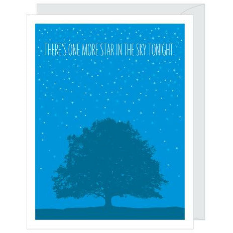 Blue greeting card with illustraions of a a large tree, all over white stars, and white text that reads "there's one more star in the sky tonight". Paired with a white envelope.