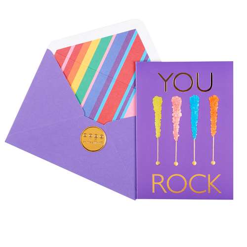 Vibrant purple greeting card, with a picture of 4 pop rock candies and text "You Rock" in gold foil, paired with a matching envelope with rainbow striped liner and a debossed gold seal