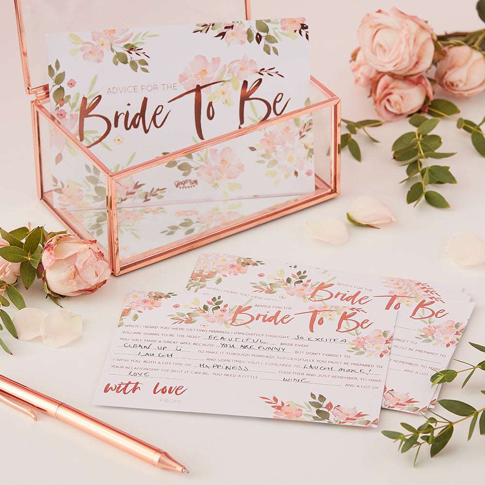 Rose gold printed floral advice cards with the text 'Bride to be' and a space for personalized advice. rose gold and glass box, pink roses, and a pen on a table.