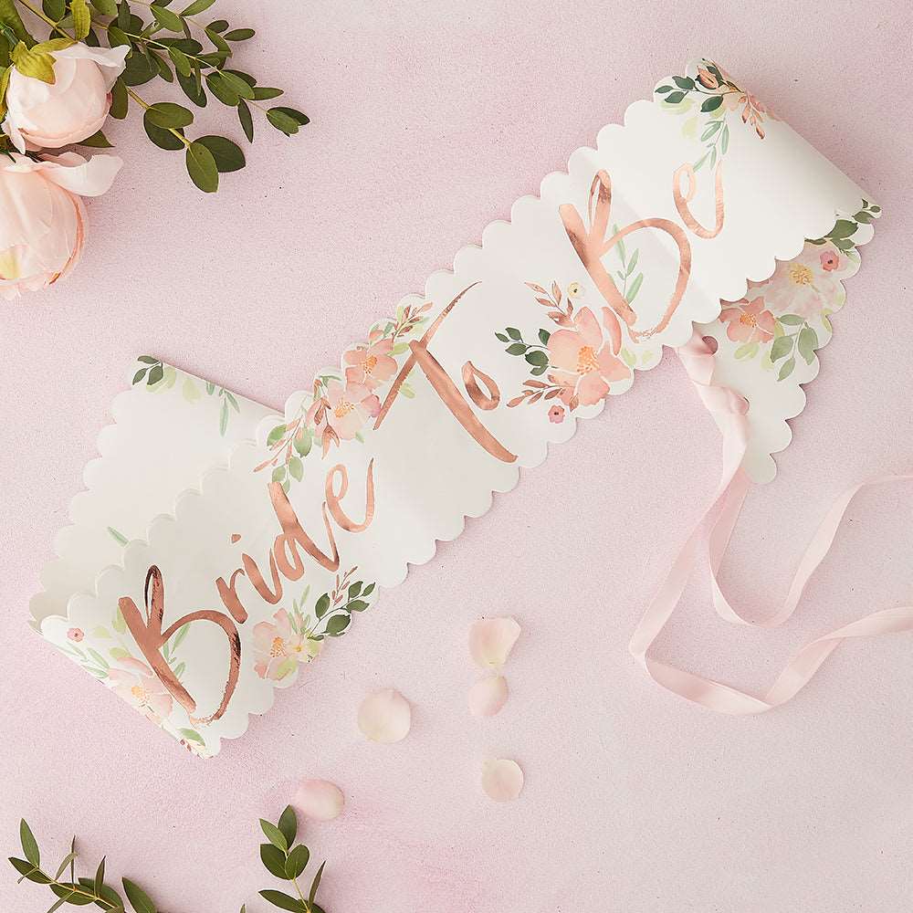 White sash with pink and green floral print, bride to be in rose gold metallic print on a pink background with pink peony flowers, petals, and greenery.