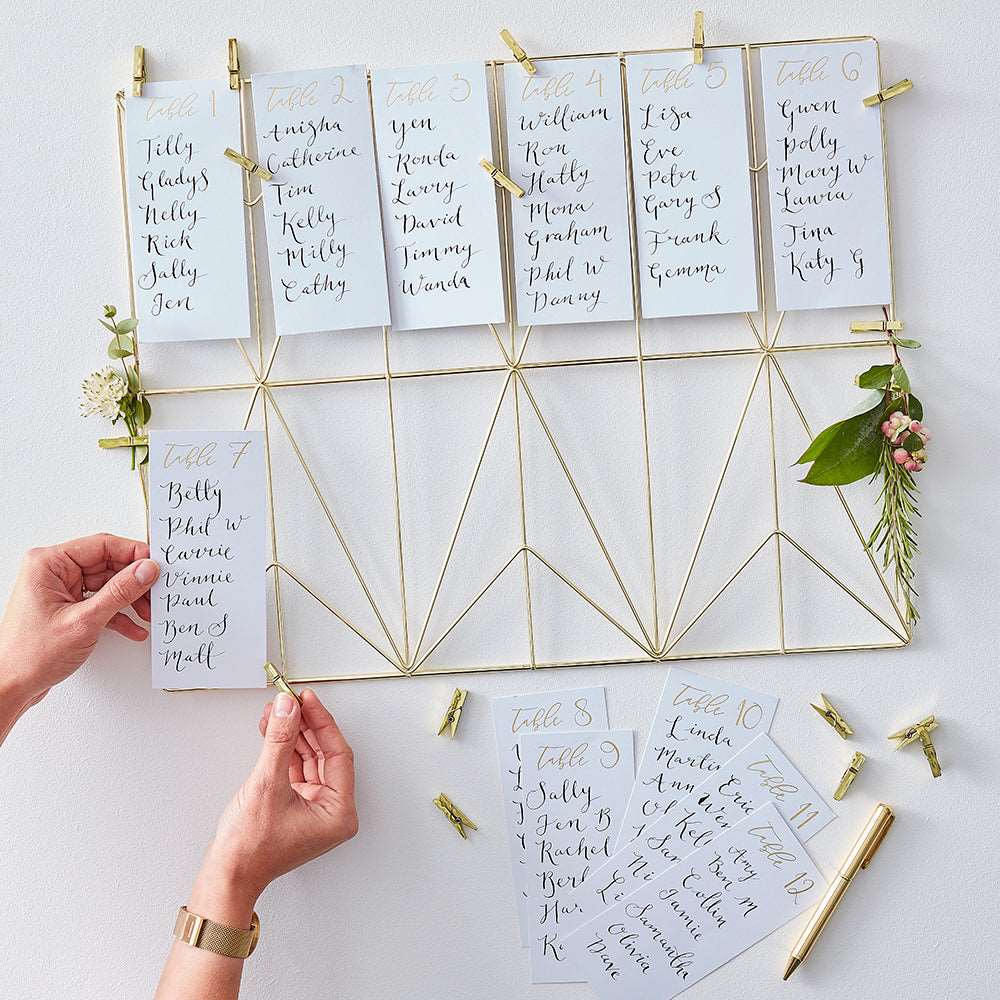 A gold wire frame on which table number cards are displayed, with the numbers 1 to 12, accompanied by small gold clothes pins for mounting.