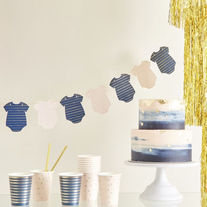 Navy and gold striped & Pink and gold polka dot baby onesie-shaped bunting banner, Navy and gold striped & Pink and gold polka dot paper cups, navy and pink cake on white stand, gold tassels