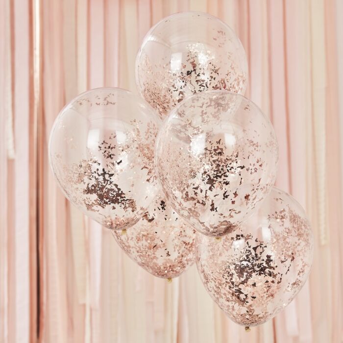A set of rose gold confetti-filled clear balloons in front of rose gold shimmer curtains