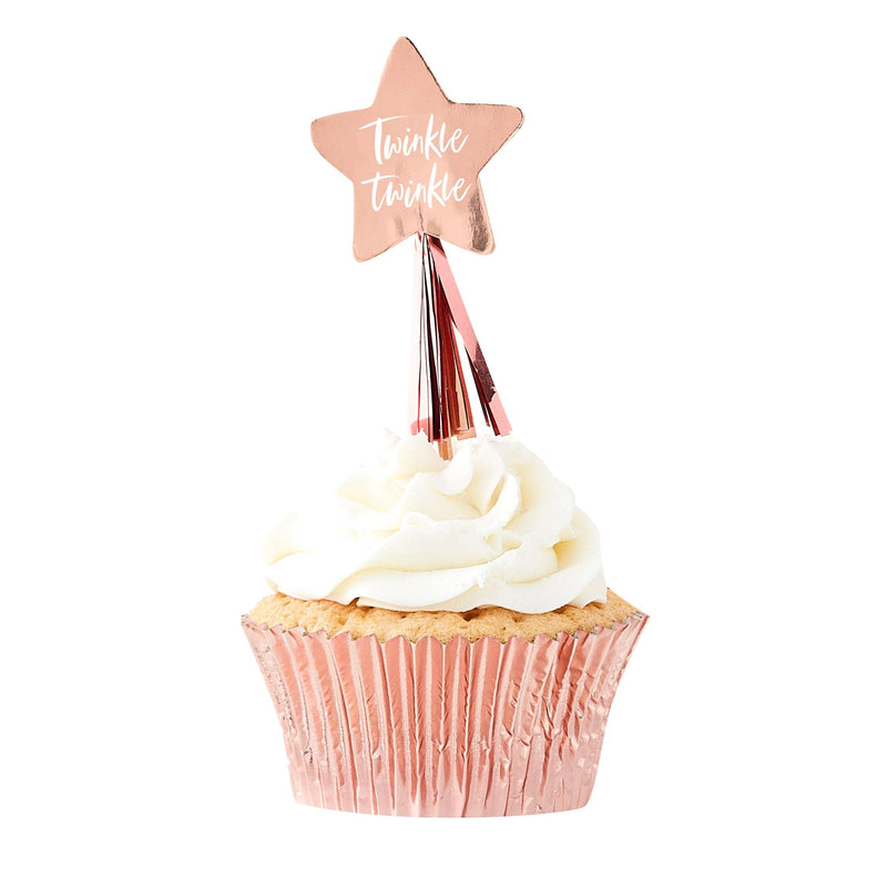 Rose gold foil, star-shaped cupcake toppers with tassels and phrase “Twinkle Twinkle” in script on the star placed on top of a cupcake.