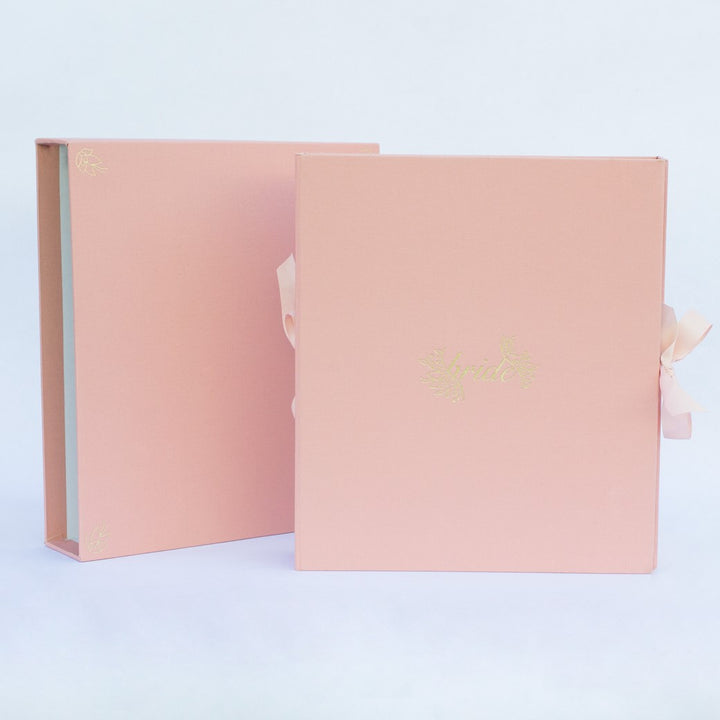 A coral pink fabric-covered wedding planner book set on a white background