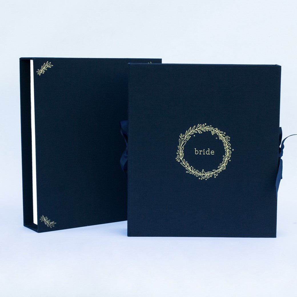 A navy fabric-covered wedding planner book set on a white background