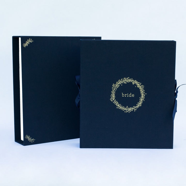 A navy fabric-covered wedding planner book set on a white background