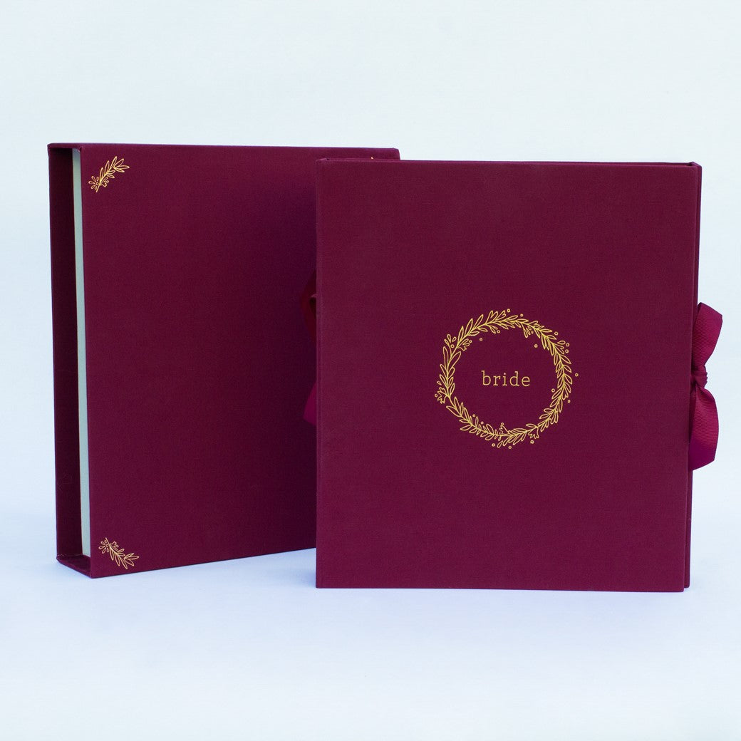A wine-burgundy fabric-covered wedding planner book set on a white background