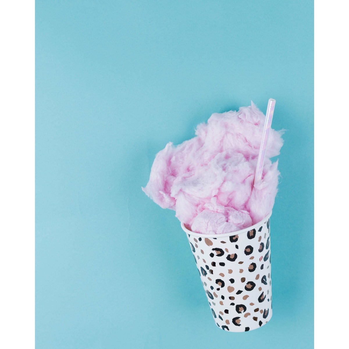 Blue background, animal print paper cup with cotton candy and an iridescent paper straw in it.