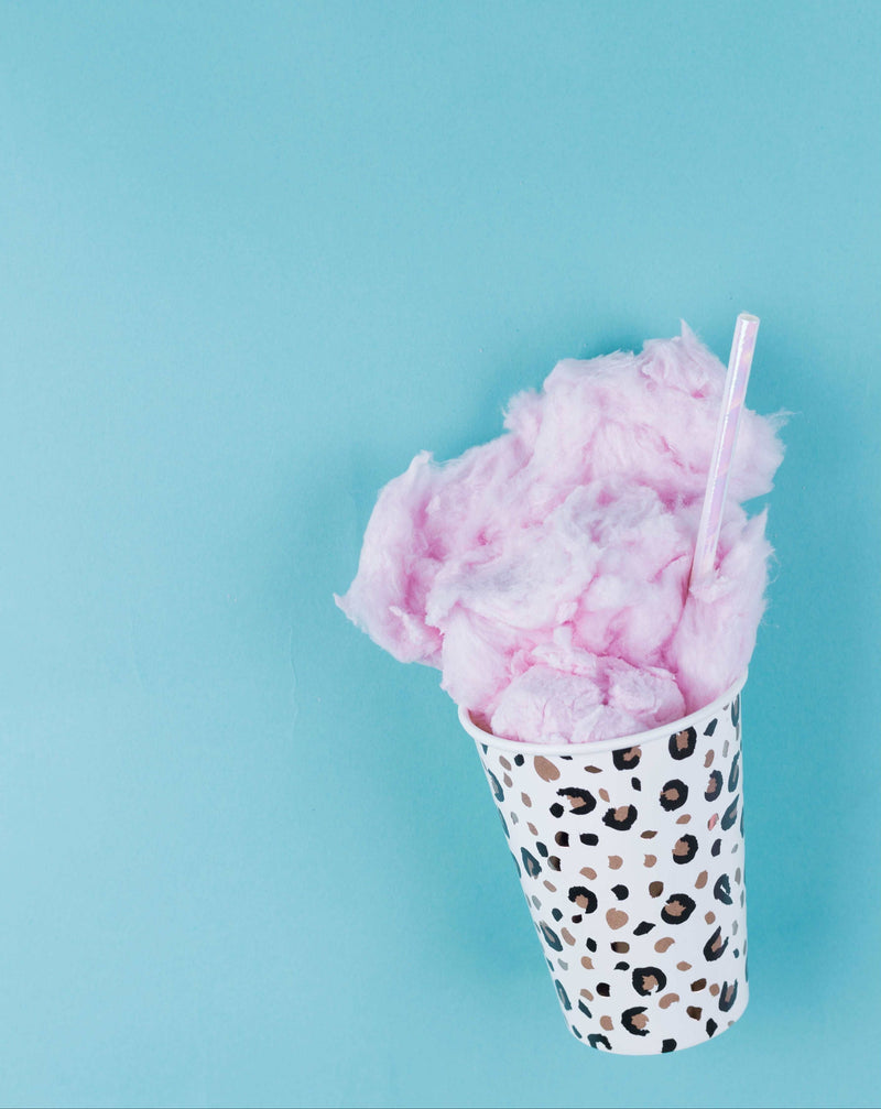 Leopard printed paper cup with cotton candy coming out of it and a pink iridescent straw on a teal blue background