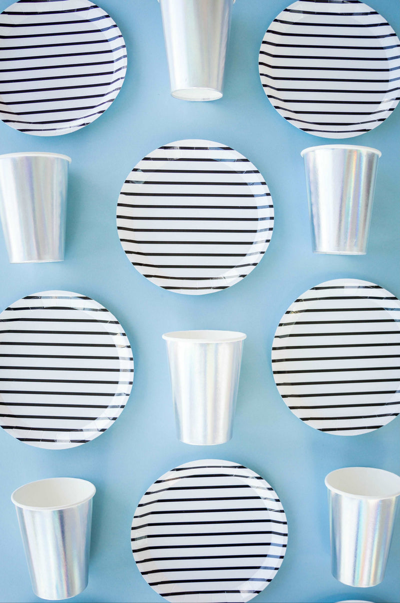White with black pinstripe party paper plates against a sky blue background with metallic silver cups