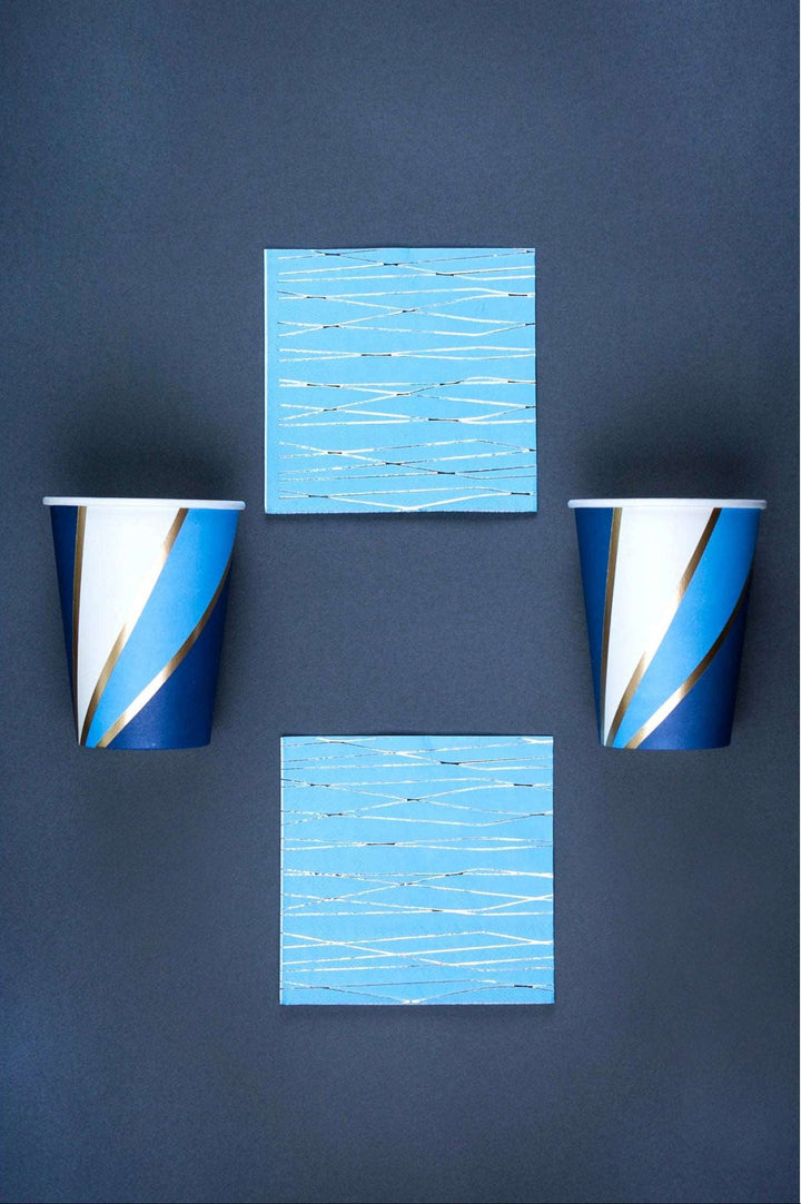 2 navy, sky blue, white, and gold foil swirl print paper cup and 2 sky blue napkin with silver foil print pattern on a navy background