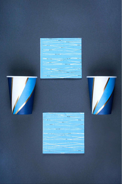 2 navy, sky blue, white, and gold foil swirl print paper cup and 2 sky blue napkin with silver foil print pattern on a navy background