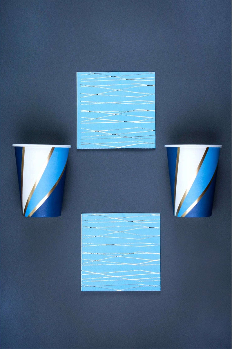 2 navy, sky blue, white, and gold foil swirl print paper cup and 2 sky blue napkin with silver foil print pattern on a navy background