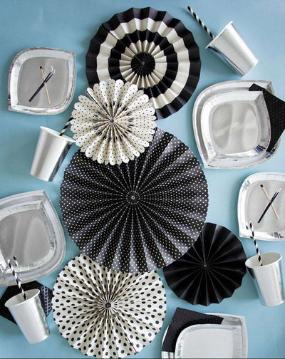 a group of silver foil charger plates, dinner plates, and cups with black and white striped drinking cups, black diamond embossed napkins, white and black printed paper wall fans