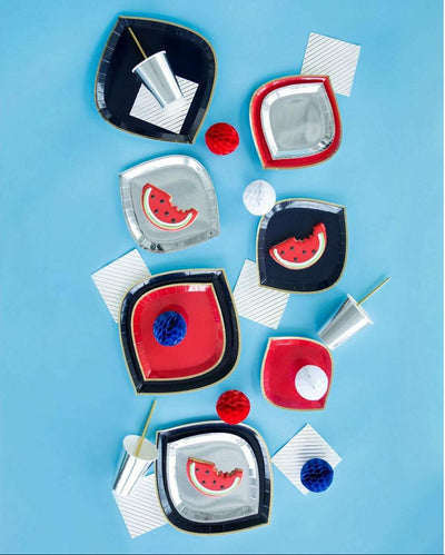 a group of navy charger plates with gold rim, red dinner plates with gold rims, and silver foil dinner plates and cups with gold drinking straws, white with gold diagonal striped napkins