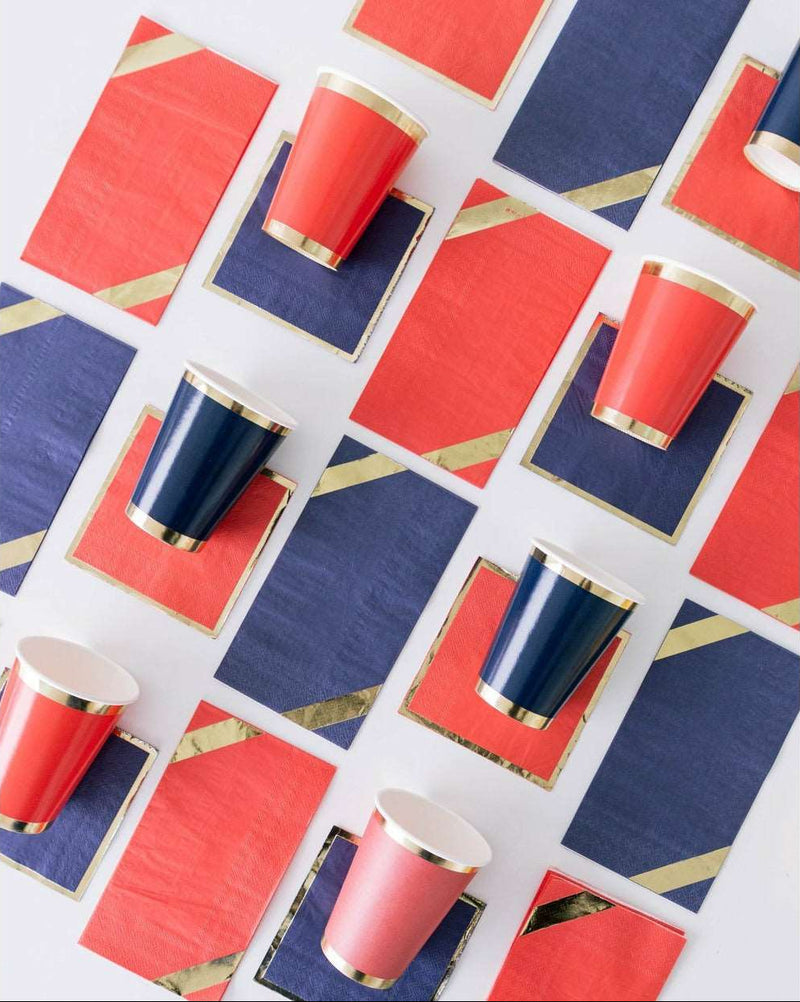 layout of alternating red dinner napkins with gold diagonal trim and navy dinner napkins with gold diagonal trim, red cocktail napkins with gold trim and navy cocktail napkins with gold trim, and red cups with gold borders and navy cups with gold borders.