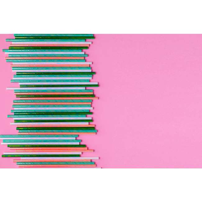 A row of iridescent foil paper straws in emerald-green, peach, white, and turquoise on a pink background