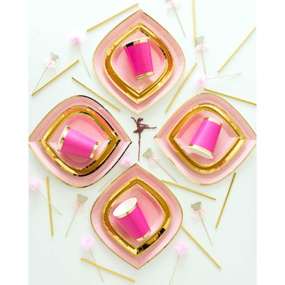 Gold foil paper straws scattered on white table around, blush pink gold rimmed paper plates with fuchsia pink gold trimmed paper cups 