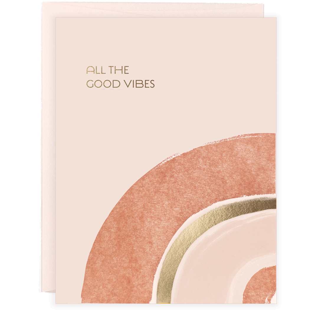 Pink greeting card with an illustrated tonal colored rainbow and the text "All The Good Vibes" in gold foil print with a matching pink envelope