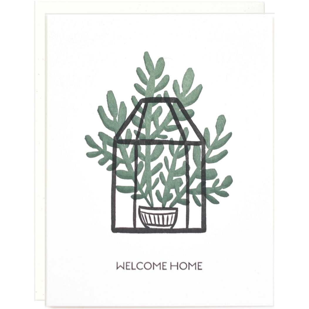 White greeting card with an illustrated houseplant in a plant pot in a terrarium, and text that reads welcome home and a white envelope