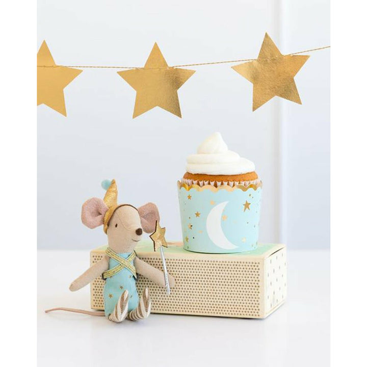 Light blue cupcake cup with a cupcake topped with vanilla frosting on top of a box. gold star banner above and a stuffed mouse toy