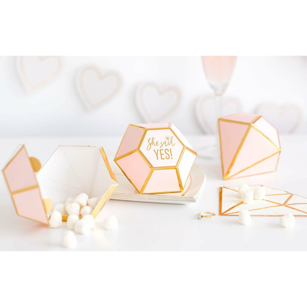 3 diamond-shaped die-cut pink favor boxes with gold foil trim detail and gold foil print that reads "she said yes" in the center. 1 favor box is open with white mint candy pouring out.