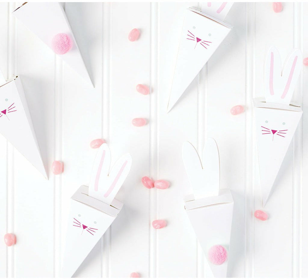 White bead board background with pink jellybeans scattered and 6 white easter bunny die cut favor boxes.