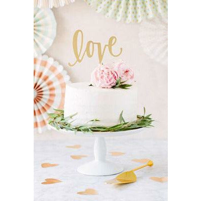 A gold cake topper with the word 'love' in a cursive script positioned on top of a multi-tiered cake decorated with pink roses and green leaves.