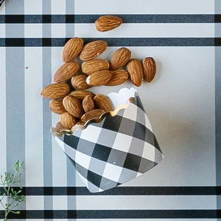 A black and white gingham plaid printed baking cup on a black and white table runner with almonds spilling out