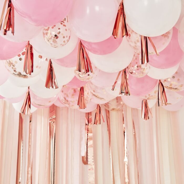 A decorative balloon ceiling arrangement featuring rose gold, pink, and white balloons with metallic rose gold tassels.
