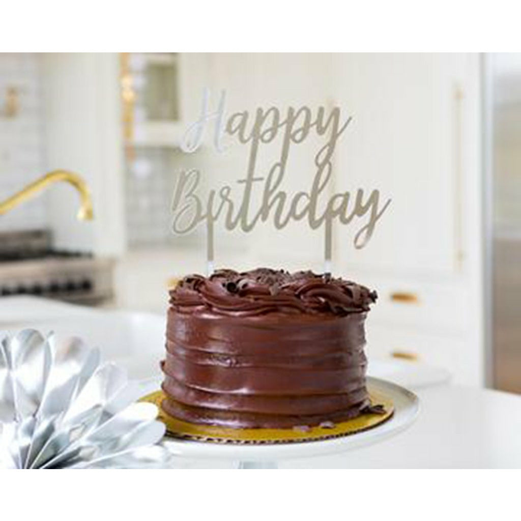 Chocolate frosted cake with a silver acrylic happy birthday cake topper with a kitchen background