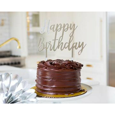 Chocolate frosted cake with a silver acrylic happy birthday cake topper with a kitchen background