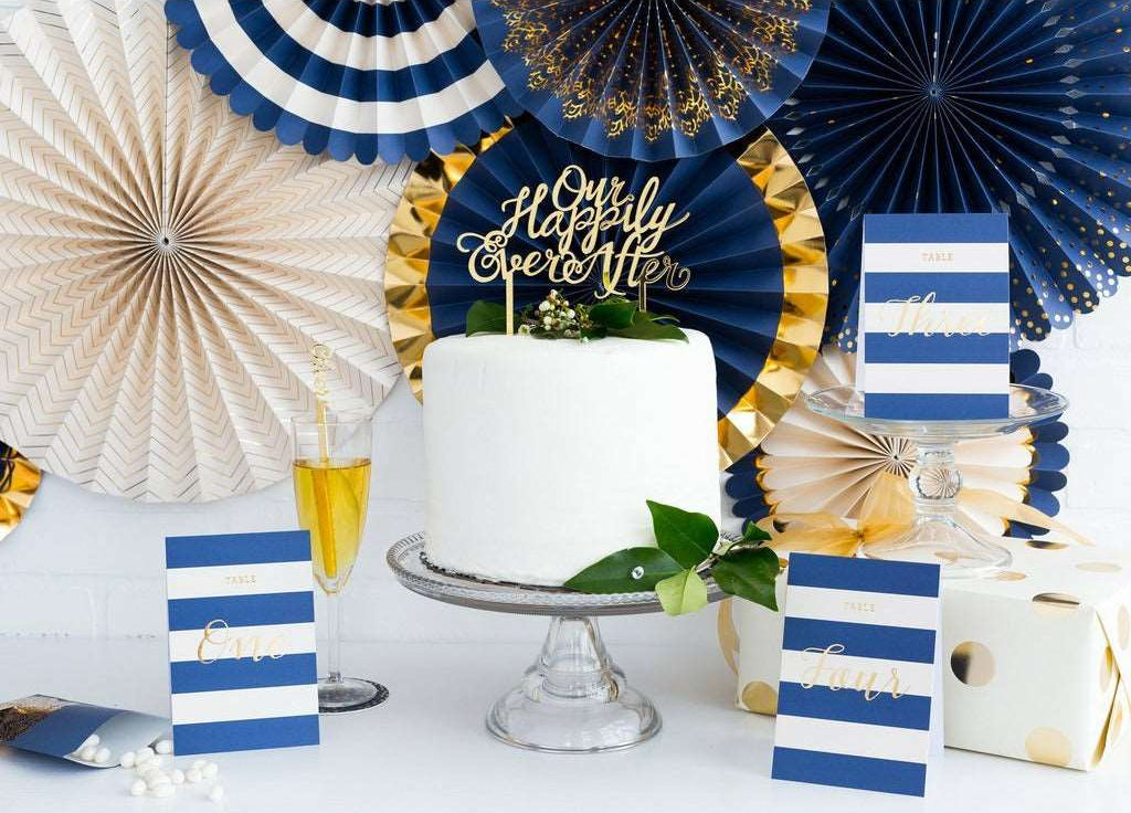 Navy and white striped table number cards surrounded by navy, white, and gold party fans.