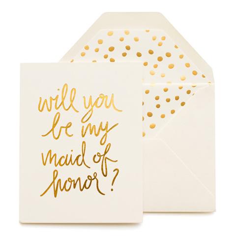 Cream greeting card with large gold foil script font that reads "Will you be my maid of honor?" Paired with a cream envelope with a gold foil polka dot envelope liner.