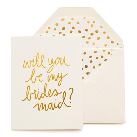 Cream greeting card with large gold foil script font that reads "Will you be my bridesmaid?" Paired with a cream envelope with a gold foil polka dot envelope liner.