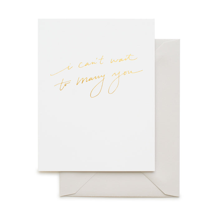A white greeting card with gold foil text that reads "I CAN'T WAIT TO MARRY YOU" in script font, along with a grey envelope.